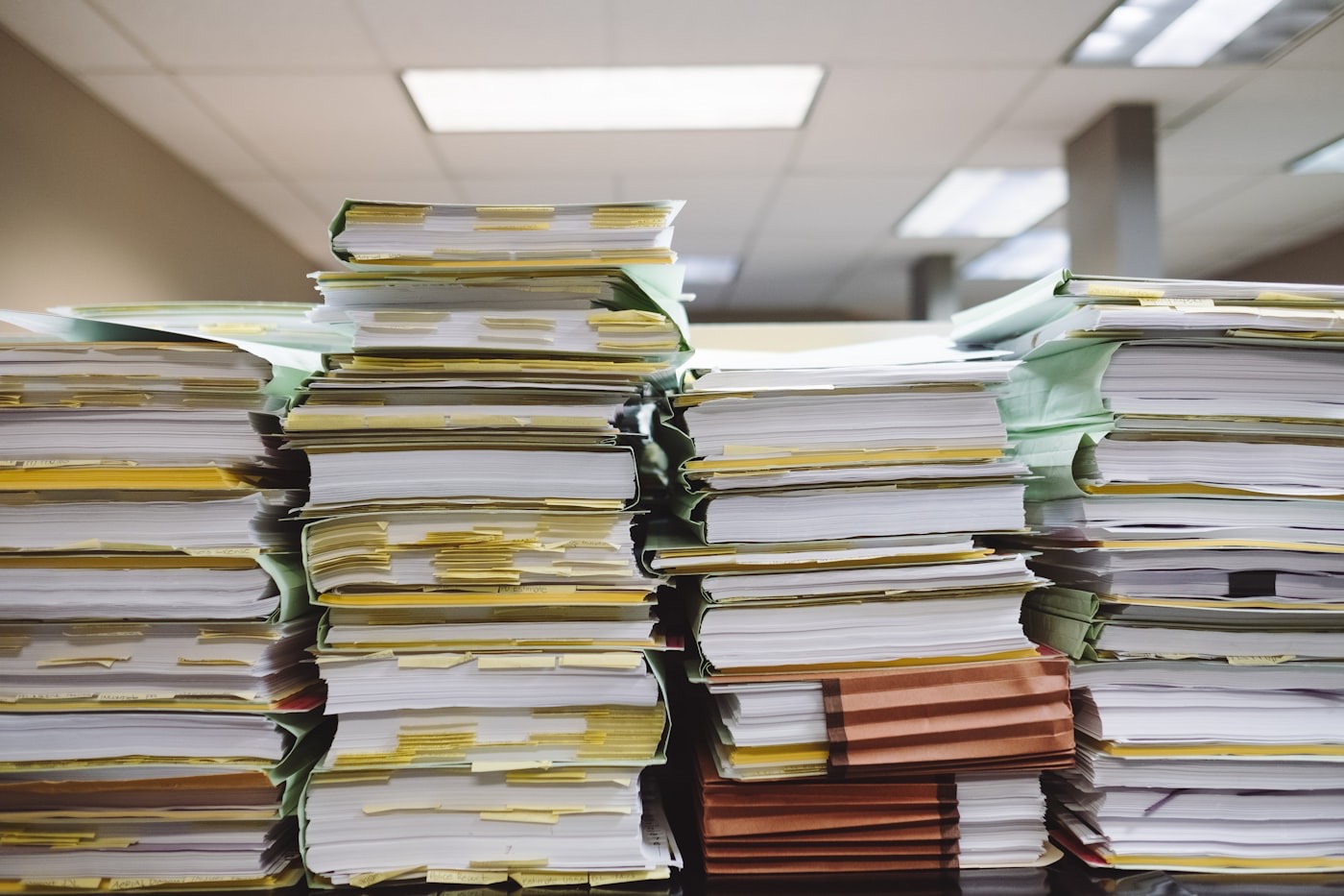 Stacks of thick document files with coloured index tabs piled on a desk